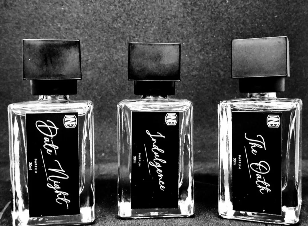 Three glass perfume bottles labeled Date Night, Indulgence, and The Oath on a dark background.